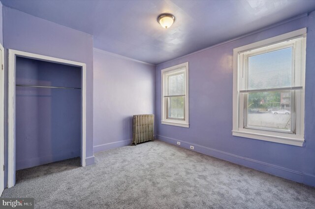 unfurnished bedroom featuring a closet, radiator heating unit, ornamental molding, carpet flooring, and baseboards