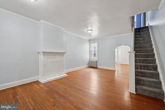 unfurnished living room with crown molding, stairway, wood-type flooring, arched walkways, and radiator heating unit