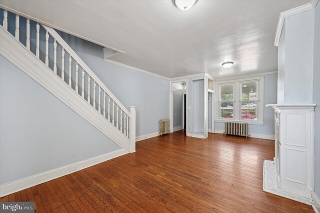 unfurnished living room featuring hardwood / wood-style floors, stairway, crown molding, and radiator