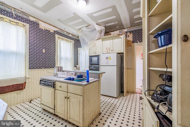 kitchen with a center island, a wainscoted wall, wallpapered walls, light floors, and black appliances