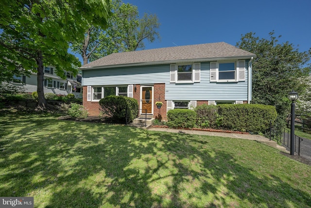 split level home featuring brick siding, fence, and a front yard