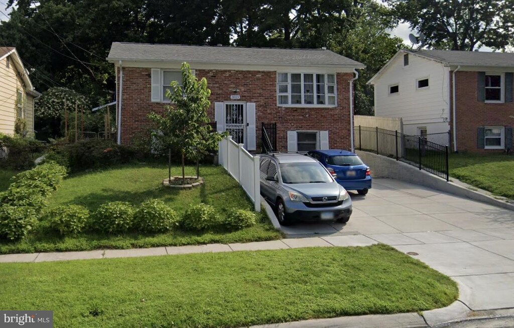 bi-level home featuring a front lawn, fence, and brick siding