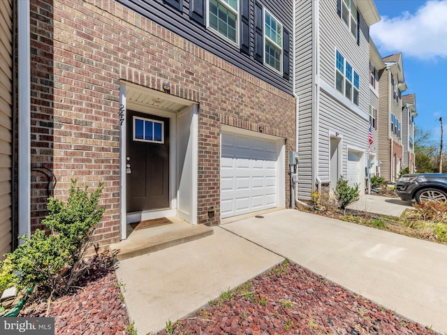 entrance to property featuring brick siding, an attached garage, and concrete driveway