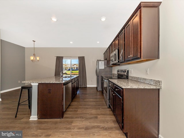 kitchen featuring a kitchen breakfast bar, appliances with stainless steel finishes, a sink, baseboards, and an inviting chandelier