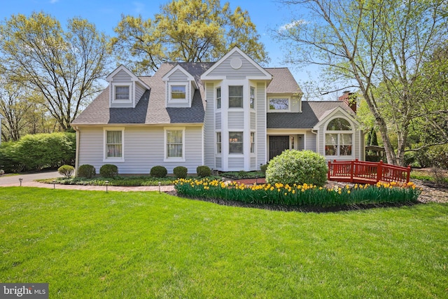 view of front of house featuring a front yard, a wooden deck, a shingled roof, and a chimney