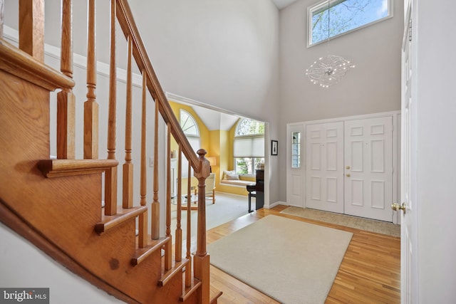 foyer entrance featuring a towering ceiling, stairway, wood finished floors, and baseboards