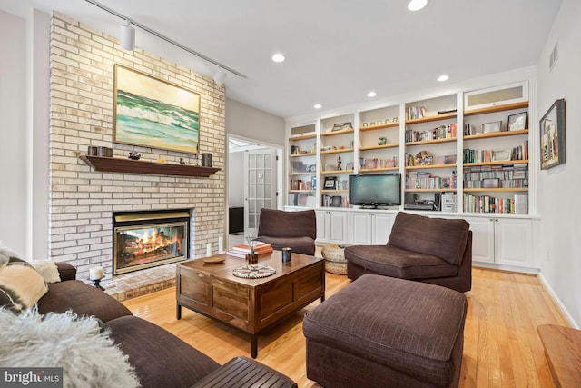 living area with light wood finished floors, a brick fireplace, rail lighting, built in features, and visible vents