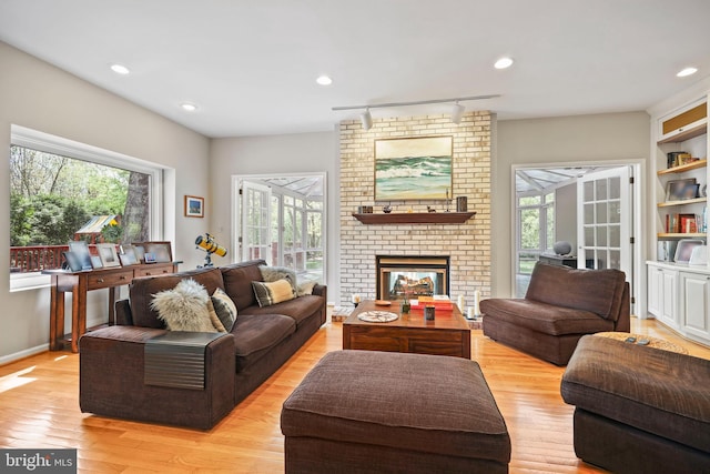 living room featuring plenty of natural light, light wood finished floors, recessed lighting, and a brick fireplace