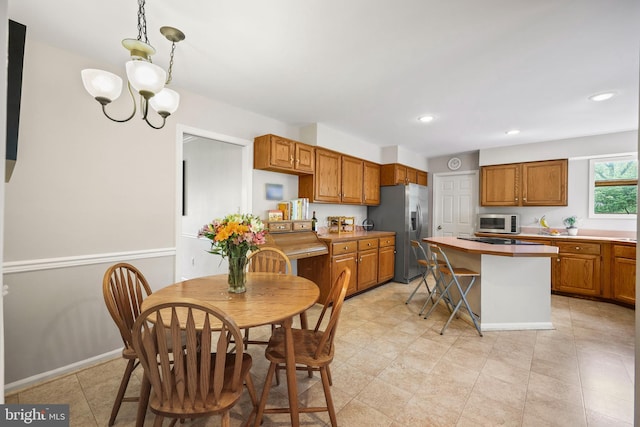 kitchen with brown cabinets, appliances with stainless steel finishes, a kitchen island, baseboards, and an inviting chandelier
