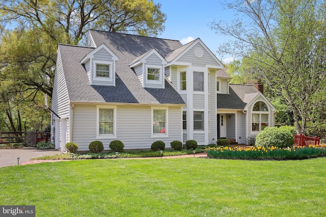 new england style home with aphalt driveway, a shingled roof, a front yard, an attached garage, and fence