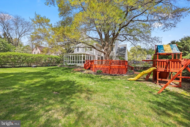 view of yard with a sunroom, a wooden deck, a playground, and fence