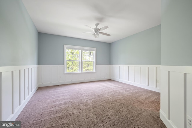 carpeted spare room featuring visible vents, wainscoting, and ceiling fan