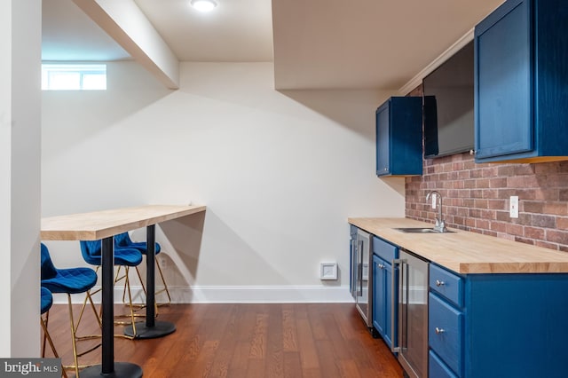 kitchen with backsplash, wooden counters, blue cabinetry, a sink, and dark wood-style floors