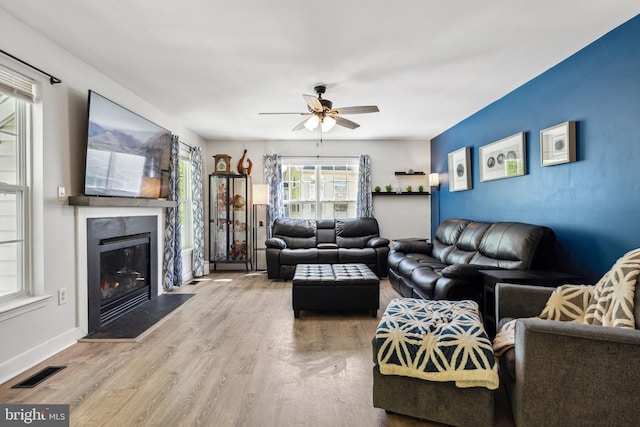 living room with wood finished floors, ceiling fan, a glass covered fireplace, baseboards, and visible vents