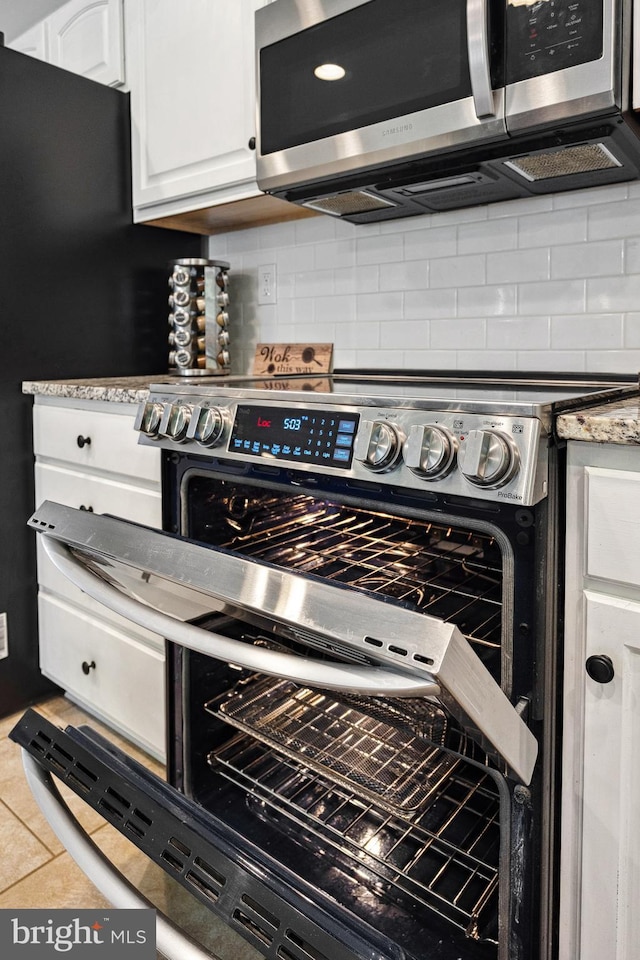 interior details featuring backsplash, white cabinets, appliances with stainless steel finishes, and light stone counters