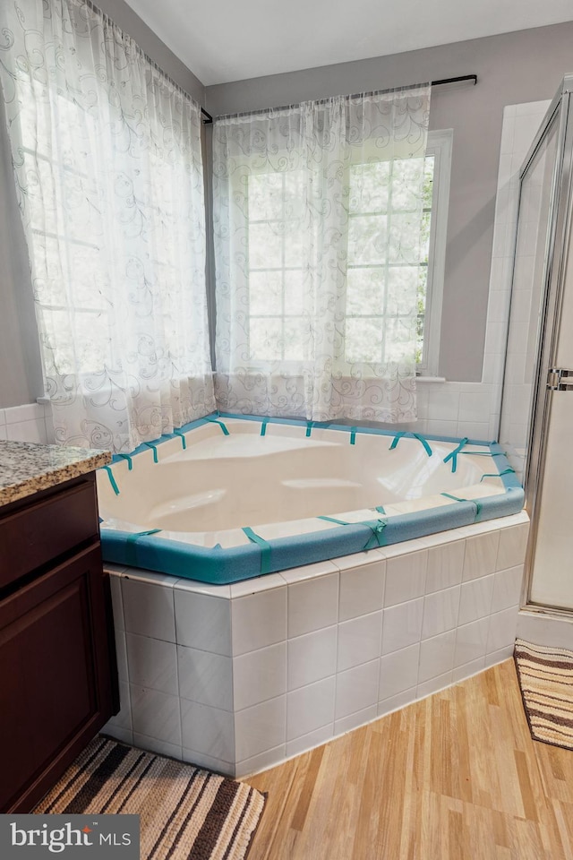 full bathroom featuring wood finished floors, a shower stall, a bath, and vanity