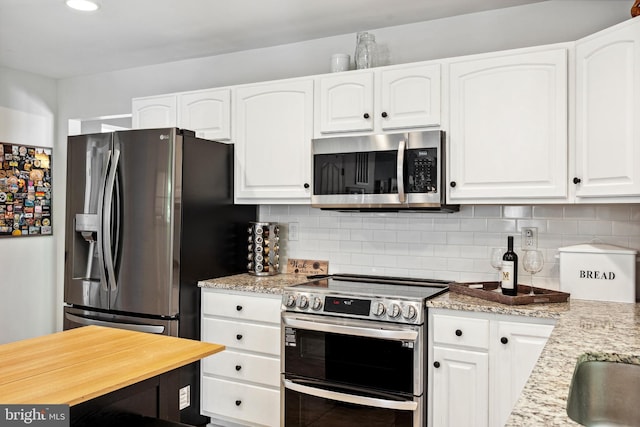 kitchen featuring white cabinets, stainless steel appliances, light stone counters, and decorative backsplash