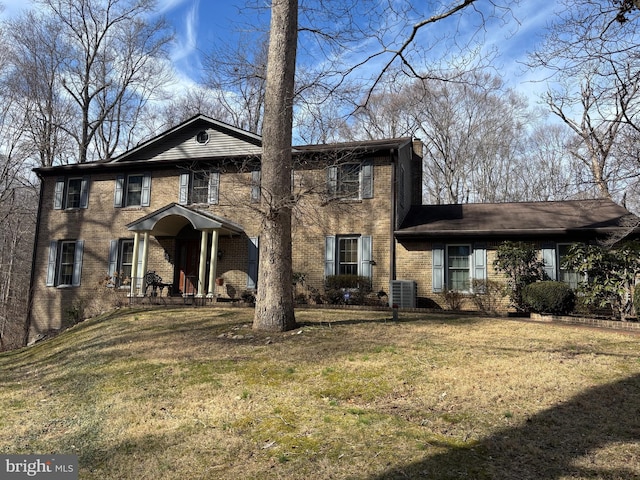 colonial home featuring a chimney, brick siding, and a front lawn