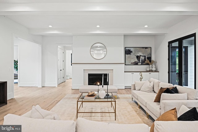 living area with beamed ceiling, recessed lighting, a glass covered fireplace, and light wood-type flooring