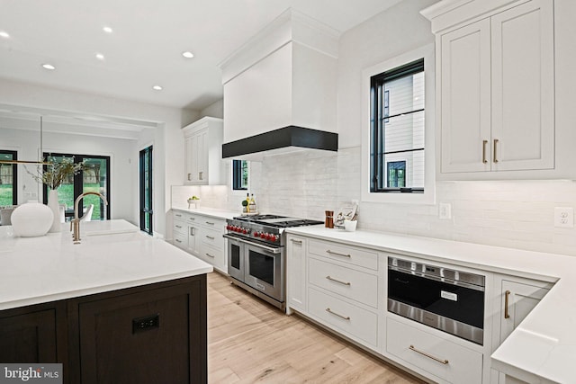 kitchen featuring double oven range, white cabinets, a sink, light countertops, and premium range hood