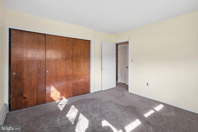 unfurnished bedroom with a closet, carpet flooring, baseboard heating, and baseboards