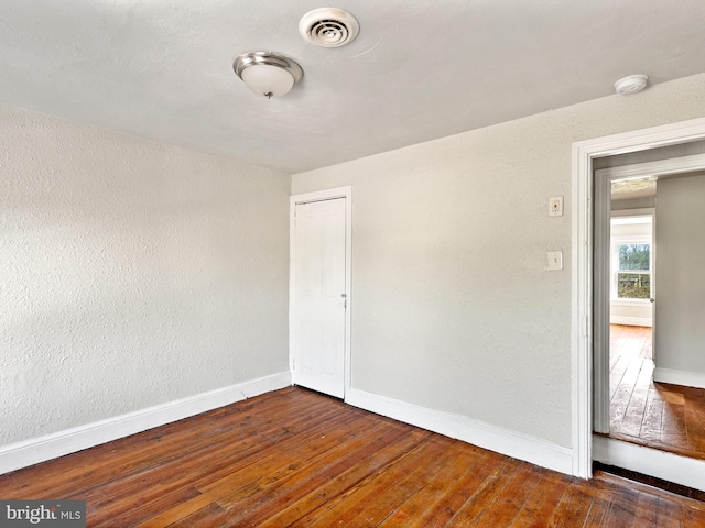 spare room featuring visible vents, hardwood / wood-style floors, a textured wall, and baseboards
