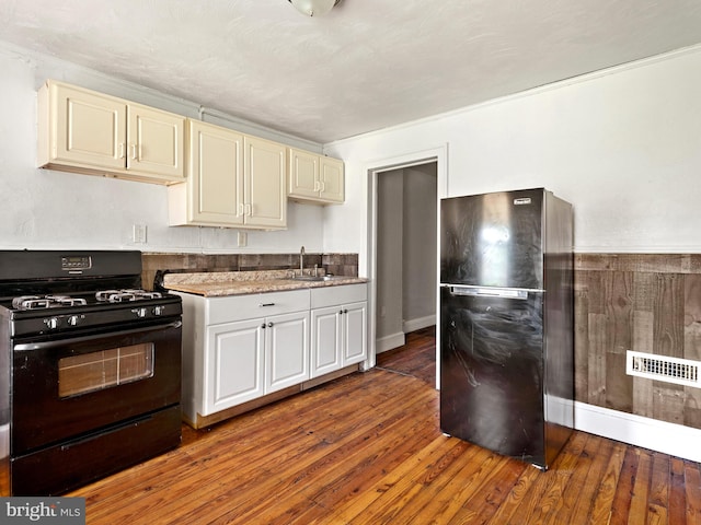 kitchen featuring freestanding refrigerator, hardwood / wood-style flooring, black gas stove, a sink, and visible vents
