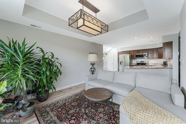 living room featuring light wood-type flooring, baseboards, recessed lighting, and a tray ceiling