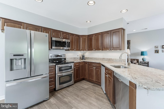 kitchen with stainless steel appliances, a sink, a peninsula, recessed lighting, and light stone countertops