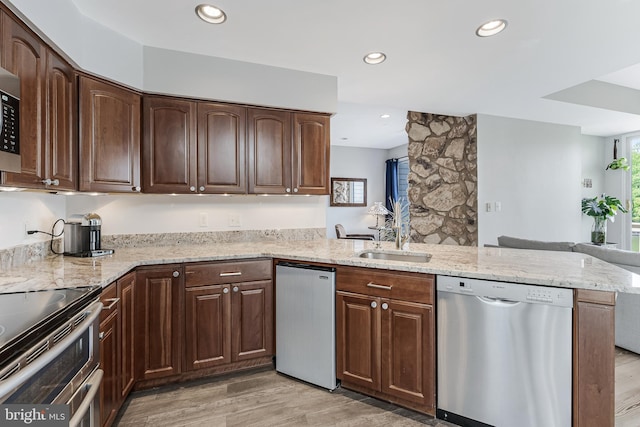 kitchen featuring appliances with stainless steel finishes, light wood-style floors, a peninsula, light stone counters, and a sink