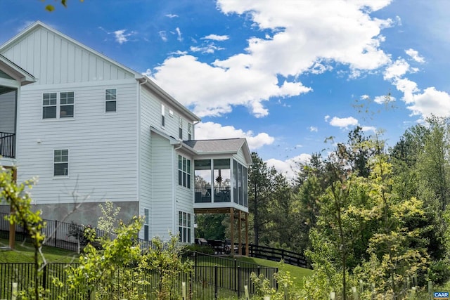 view of side of home with a sunroom, board and batten siding, fence, and a lawn