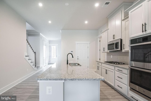 kitchen featuring a sink, light wood-type flooring, tasteful backsplash, visible vents, and appliances with stainless steel finishes