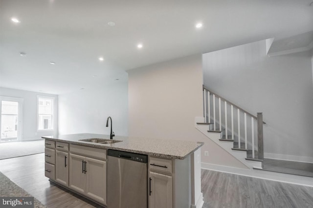 kitchen with light stone countertops, stainless steel dishwasher, a sink, light wood-type flooring, and a center island with sink