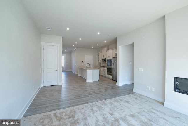 unfurnished living room with a sink, visible vents, baseboards, light wood-type flooring, and recessed lighting