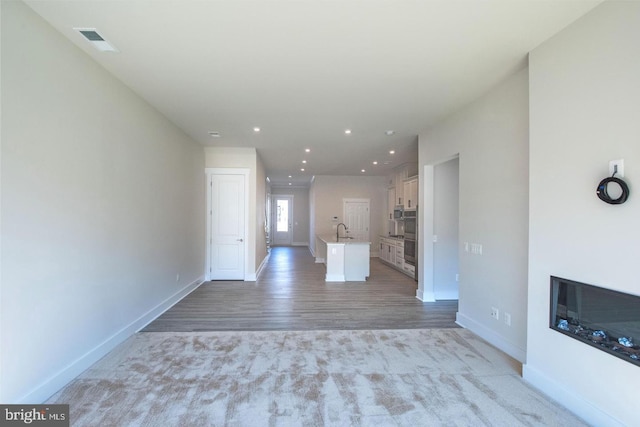 unfurnished living room featuring a sink, visible vents, light wood-style flooring, and baseboards