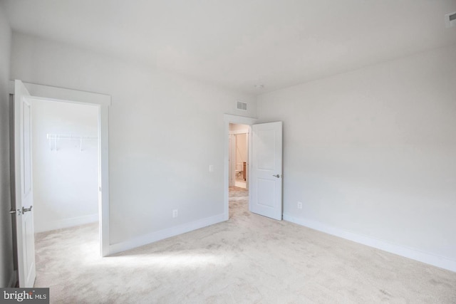 unfurnished bedroom featuring visible vents, a closet, baseboards, carpet, and a walk in closet
