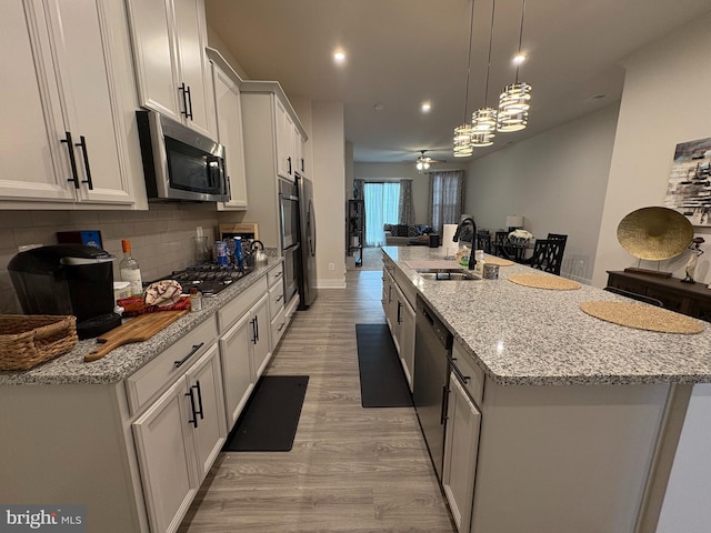 kitchen with tasteful backsplash, stainless steel appliances, a large island with sink, a sink, and light wood-type flooring