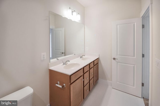 bathroom with toilet, double vanity, a sink, and baseboards