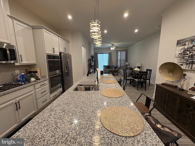 kitchen featuring recessed lighting, a sink, stainless steel appliances, wood finished floors, and open floor plan