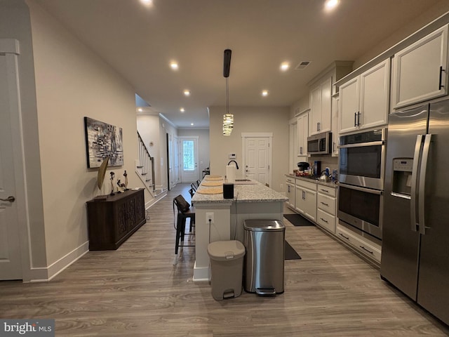 kitchen featuring a kitchen island with sink, a sink, stainless steel appliances, visible vents, and baseboards