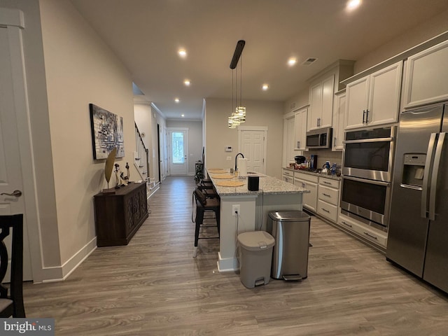 kitchen with recessed lighting, wood finished floors, a breakfast bar area, stainless steel appliances, and baseboards