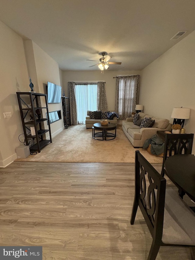 living room with a ceiling fan, visible vents, wood finished floors, and baseboards