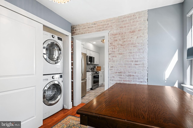clothes washing area featuring stacked washer / drying machine, laundry area, and brick wall