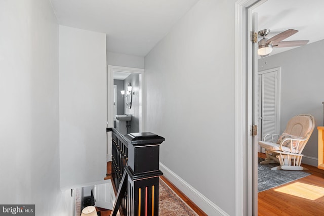 corridor with baseboards, an upstairs landing, and wood finished floors