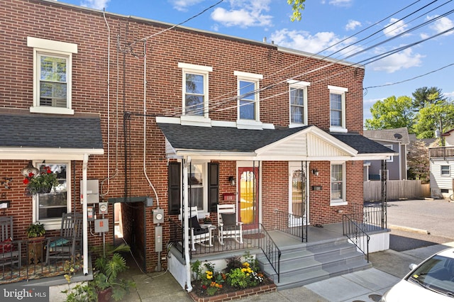 view of front of property with brick siding, roof with shingles, and fence
