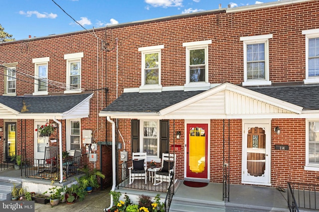 multi unit property featuring a shingled roof, a porch, and brick siding
