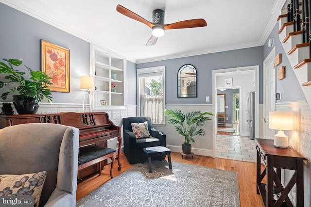 living area with crown molding, stairs, a ceiling fan, baseboards, and wood finished floors