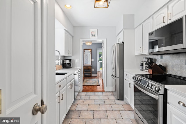 kitchen featuring appliances with stainless steel finishes, a sink, light countertops, white cabinetry, and decorative backsplash