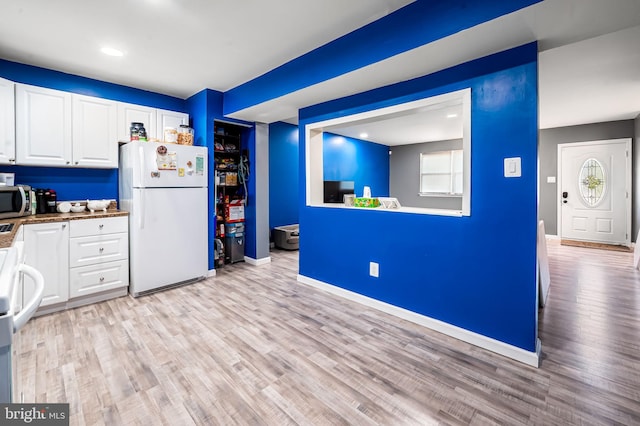 kitchen featuring baseboards, stainless steel microwave, freestanding refrigerator, light wood-style floors, and white cabinetry