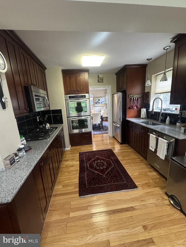 kitchen with appliances with stainless steel finishes, light wood-style floors, dark brown cabinets, and a sink